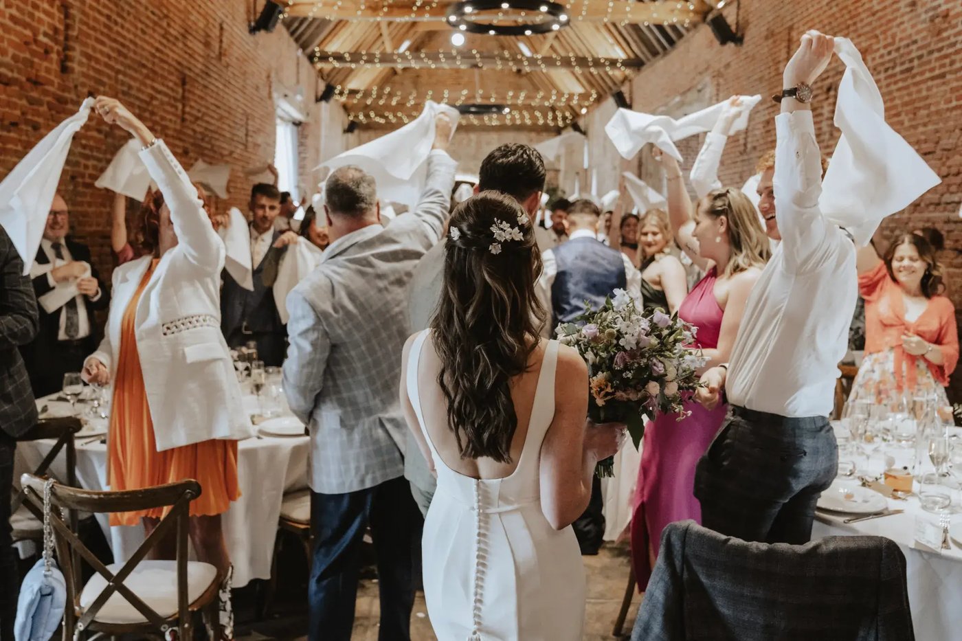 Couple entering their wedding breakfast with guests waving napkins at Copdock Hall